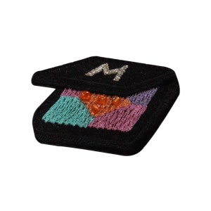 May include: Black embroidered patch with a colourful geometric design and a silver letter "M" in the centre.
