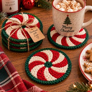Puede incluir: Un juego de posavasos redondos de ganchillo con un patrón de espiral de menta en rojo, blanco y verde. Los posavasos están apilados y atados con cordel, con una etiqueta que dice Handmade with Love, y uno bajo una taza.