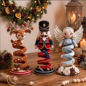 Puede incluir: Tres figuras de ganchillo sobre bases en espiral: un ciervo marrón con astas, un cascanueces con uniforme rojo y azul, y un ángel azul claro con alas. Cada figura se asienta sobre una base circular decorada con elementos festivos.