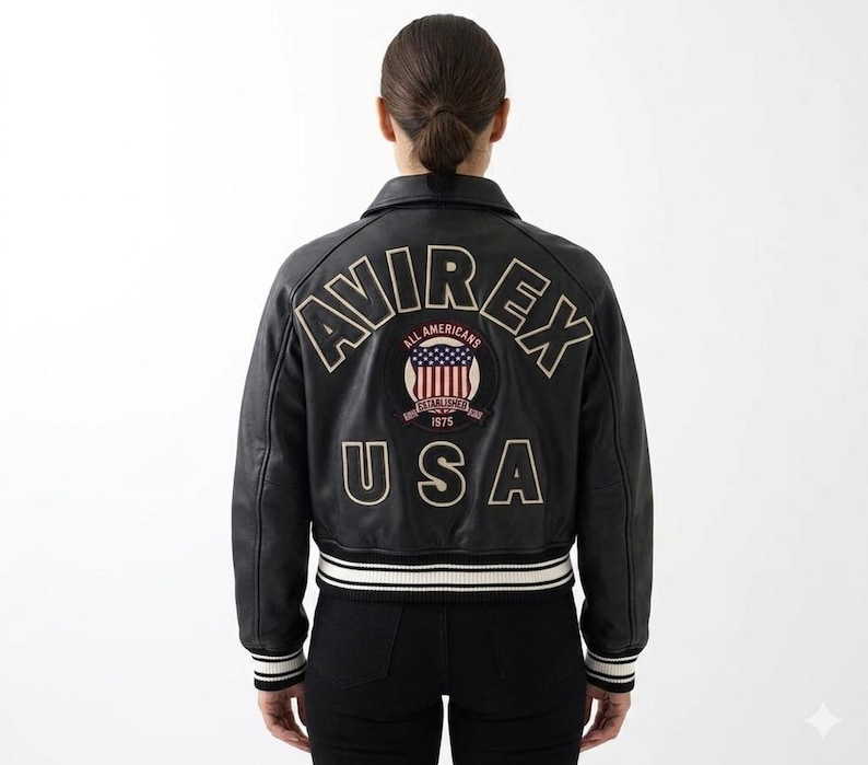 May include: A black leather varsity jacket featuring the text AVIREX in an arched font and USA in a straight font on the back. A circular patch in the center displays the text ALL AMERICANS ESTABLISHED 1975 with a graphic of the American flag.