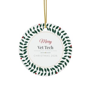 Könnte beinhalten: Ein rundes, weißes Keramikornament, das an einer goldenen Schnur hängt. Das Ornament hat einen grünen Blätterkranz-Rand mit kleinen roten Beeren und goldenen Sternen. Der mittlere Text lautet Merry Vet Tech POWERED BY COFFEE & PAWS CHRISTMAS 2026.