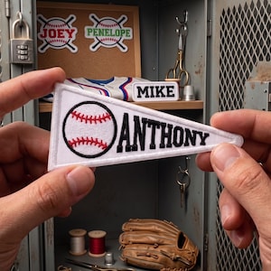 May include: A white triangular pennant patch featuring a black and red embroidered baseball graphic on the left and the name ANTHONY in black block lettering on the right, with a white border and a clean, finished edge for attachment.