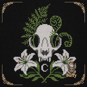 May include: A cross-stitch pattern on black fabric featuring a white animal skull centered among green fern fronds and two white lilies. Below the skull is a small white letter C. A small bat illustration with the text The Big Buffy is visible.