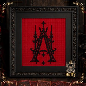 Può includere: Un ricamo a punto croce incorniciato che presenta una lettera A nera in stile gotico centrata su uno sfondo di tessuto rosso vibrante. L'opera è racchiusa in una cornice nera decorata con dettagli intricati e include un logo The Big Buffy.