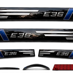 May include: A set of four black rectangular door sill plates featuring the silver text E36, three horizontal silver stripes, and a blue diagonal accent. The set includes two long and two short pieces, with a red adhesive backing shown on one.
