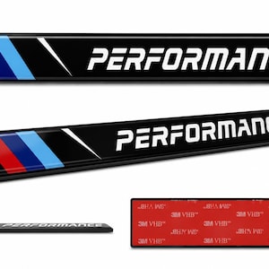 May include: A rectangular black emblem featuring the word PERFORMANCE in white capital letters. The left side displays three diagonal stripes in red, dark blue, and light blue. The back side shows a red adhesive backing with 3M VHB text.