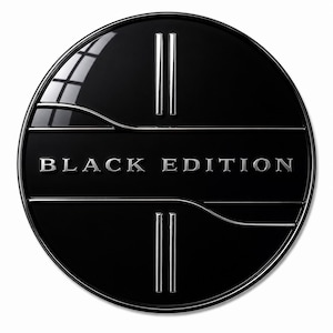 Könnte beinhalten: Ein kreisförmiges schwarzes Emblem mit glänzender Oberfläche und dem mittig platzierten silbernen Schriftzug BLACK EDITION. Das Design zeigt zwei Sätze vertikaler silberner Parallellinien oben und unten, die von einer horizontalen Wellenlinie durchschnitten werden.