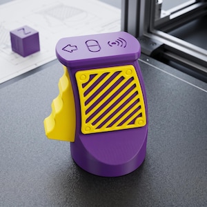 May include: A purple and yellow handheld controller featuring a yellow side grip with a textured surface. The top surface displays an arrow icon, a pill-shaped button, and a wireless signal icon. A yellow square panel with diagonal slats is attached.