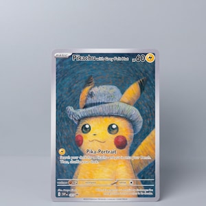 May include: A Pokémon trading card featuring Pikachu wearing a grey felt hat. The card has a yellow and grey color scheme with the text "Pikachu with Grey Felt Hat" at the top. The card also includes the text "Pika-Portrait".