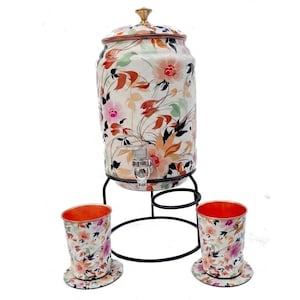 May include: A cylindrical beverage dispenser with a floral pattern in shades of pink, orange, and black, featuring a metal lid, a spigot, and a black wire stand. Two matching tumblers with floral designs and copper-colored interiors are included.