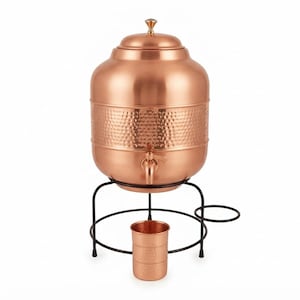 May include: A copper water dispenser with a hammered texture, a matching lid, and a spigot. The dispenser rests on a black metal stand that includes a circular holder for a matching copper tumbler, which is positioned in front of the stand.