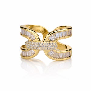 May include: A gold ring with an intricate, interwoven design. The ring is adorned with many clear, rectangular-cut and round-cut gemstones. The gemstones are set in a continuous pattern, creating a sparkling effect. The ring is displayed on a white background.