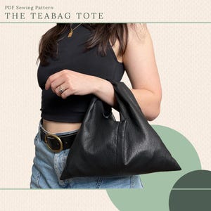 May include: Black leather tote bag with a triangular shape, held by a person. The bag has a textured surface and a simple design. The text "THE TEABAG TOTE" is at the top of the image, along with "PDF Sewing Pattern".