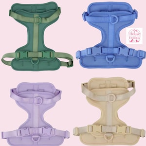 May include: Four pet harnesses in sage green, periwinkle blue, lavender, and beige. Each harness features adjustable nylon straps, plastic side-release buckles, and metal D-rings for lead attachment. A logo with the text House and Hounds is visible.