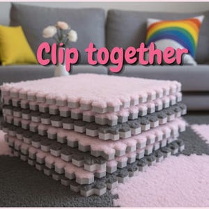 May include: A stack of square interlocking foam floor tiles with a soft, fuzzy texture. The tiles alternate between light pink and dark gray colors. The text "Clip together" is written in pink letters across the center of the image.