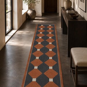 May include: A long rectangular runner rug featuring a repeating geometric pattern of dark charcoal gray diamonds and burnt orange diamonds separated by small white squares, all enclosed within a solid burnt orange border frame.