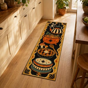 May include: A long rectangular runner rug featuring a black background with a decorative border in yellow and orange. The design includes a striped teapot, an orange cauldron, mushrooms, a wooden spoon, a lattice-top pie, and a layered cake.