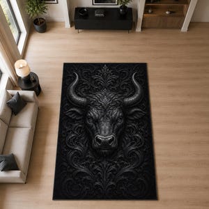 May include: A rectangular area rug featuring a large, centred black bull head in high relief. The design is surrounded by intricate, symmetrical black scrollwork and acanthus leaf patterns that extend to the edges of the rug's dark surface.