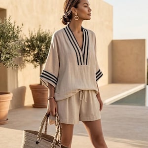 Peut inclure: Ensemble en lin beige composé d'un haut et d'un short, avec des rayures noires sur l'encolure et les manches. Le short a une taille élastique. Un sac fourre-tout tissé avec des anses marron est tenu à la main.
