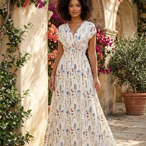 Peut inclure: Une robe blanche à imprimé floral avec un col en V et des manches courtes. La robe présente un corsage ajusté et une jupe fluide. Le motif floral comprend des fleurs rouges, bleues et jaunes. La robe est portée à l'extérieur dans un jardin.