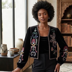 Peut inclure: Veste en velours noir avec broderies florales colorées. La veste a des manches longues et une coupe ajustée. La broderie comprend des accents roses, bleus, verts et jaunes. La veste est portée sur un haut noir et associée à un pantalon noir.