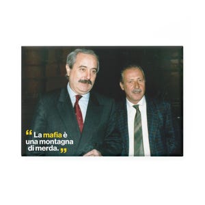 Può includere: Magnete rettangolare con due uomini in abito. Uno indossa un abito scuro con cravatta a fantasia rossa, l'altro una giacca a scacchi e cravatta verde. Testo italiano: "La mafia è una montagna di merda."