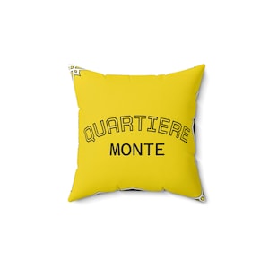 Può includere: Un cuscino quadrato giallo con la scritta nera "QUARTIERE MONTE" ad arco. Il cuscino ha un design semplice ed è probabilmente destinato all'arredamento della casa.