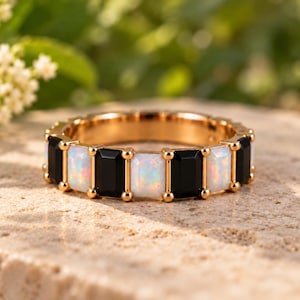 May include: A gold band ring featuring an alternating pattern of rectangular, iridescent white opal stones and solid black onyx stones. The stones are set in a gold metal frame with small gold prongs securing each individual gemstone in place.