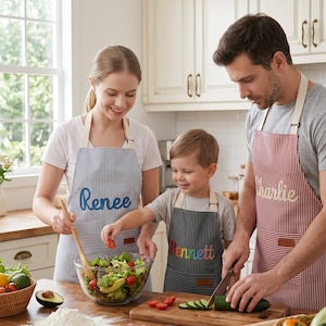 Può includere: Tre grembiuli personalizzati con cinturini regolabili al collo e tasche frontali. Un grembiule a righe blu e bianche riporta il nome Renee, un grembiule a righe nere e bianche il nome Bennett e un grembiule a righe rosse e bianche il nome Charlie.