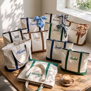 Può includere: Una collezione di borse tote in tela color bianco sporco con bordi e manici colorati. Ogni borsa presenta ricami personalizzati con nomi come Crystal, SH, Bride, Laura, Marina, Jessica, Teresa, Kristin, Sarah, Isabel e Beitha, oltre a fiocchi.