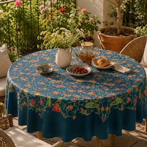 Può includere: Una tovaglia rotonda con una base blu profondo e un vivace motivo floreale ripetuto nei toni del rosa, arancione e verde. Il design presenta dettagli intricati a forma di vite e un bordo decorativo che ricade lungo il lato del tavolo.