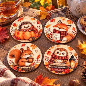 Może przedstawiać: Zestaw czterech okrągłych podkładek z jesiennymi ilustracjami. Przedstawiają jeża w dyni, lisa z kubkiem z napisem Hello Autumn, wiewiórkę z żołędziem oraz sowę na książkach z napisami Good Days, Cozy Moments, Happy Life.