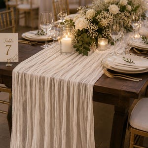 May include: A beautifully set table for a wedding or event. The dark wood table is adorned with white linens, floral arrangements, candles, and place settings. Table number 7 is displayed on the table.