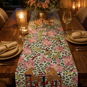 Peut inclure: Un chemin de table blanc orné d'un motif répétitif de fleurs roses, de taches de léopard vertes et d'illustrations de deux léopards assis à une petite table ronde sur des chaises rouges, buvant des bouteilles face à face sur la table.
