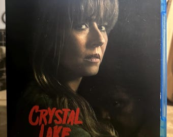 May include: A blue Blu-ray case featuring a dark cover with a person looking forward, partially obscured by shadows. The text Crystal Lake is printed in a bold, red, distressed font in the lower left corner of the cover art.