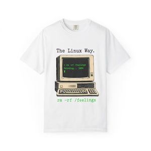 Op de afbeelding: Een wit t-shirt met korte mouwen en een afbeelding van een vintage computermonitor en toetsenbord. Het scherm toont de tekst "The Linux Way." en "> rm -rf /feelings Deleting... 100%" in het groen. Onder het toetsenbord staat "rm -rf /feelings".