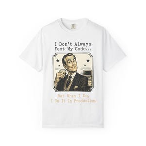 May include: White t-shirt featuring a vintage-style illustration of a man holding a drink, with the text "I Don't Always Test My Code... But When I Do, I Do It In Production." The design includes a retro frame and stars.