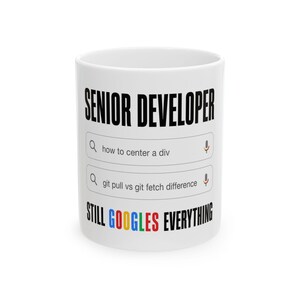 May include: A white ceramic mug featuring the black text SENIOR DEVELOPER at the top, two search bar graphics with the text how to center a div and git pull vs git fetch difference, and the text STILL GOOGLES EVERYTHING in multicolored letters.