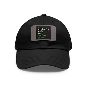 May include: Black baseball cap with a curved brim. A rectangular patch on the front displays the text "Probably Safe to Deploy" in white and green, with a coding-style symbol.