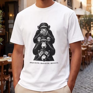Op de afbeelding: Een wit T-shirt met korte mouwen en een zwarte afbeelding van drie op elkaar gestapelde apen die hun ogen, oren en mond bedekken. Onder de illustratie staat de tekst: SPEAK NO EVIL . HEAR NO EVIL . SEE NO EVIL. Het ontwerp is in het midden geplaatst.
