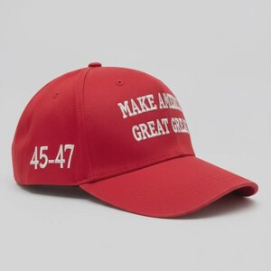 May include: A red baseball cap featuring white embroidered text on the front that reads MAKE AMERICA GREAT AGAIN and the numbers 45-47 embroidered in white on the side. The cap has a structured crown, a curved brim, and a button on the top center.
