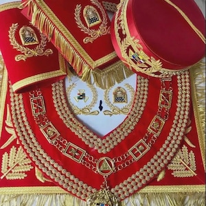 May include: A set of red velvet masonic regalia including a square apron with gold fringe and embroidery, a matching collar with gold metal emblems, a pair of cuffs with gold trim, and a round red hat featuring gold embroidery and a gold cord.