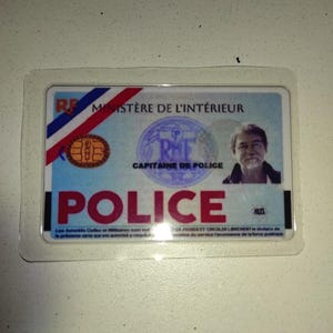 Puede incluir: Una tarjeta de identificación de la policía francesa en un estuche de plástico transparente. La tarjeta presenta los colores de la bandera francesa, un sello y la palabra "POLICE". Se ve la foto de un hombre.