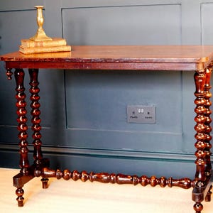 May include: A dark wood console table with turned legs and a rectangular top. A brass candlestick and two books sit on the table. The table's legs have a distinctive bobbin design. The table is approximately 76 cm long.