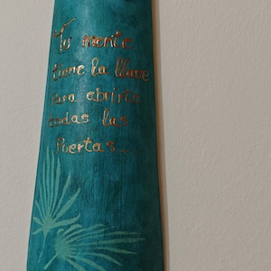 Può includere: Targa in legno turchese con il testo spagnolo "Tu mente tiene la llave para abrirte todas las puertas..." in lettere dorate. La targa presenta un disegno di foglie di palma e due fori nella parte superiore per appenderla.