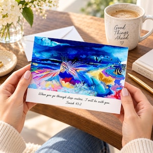 May include: A rectangular greeting card featuring a vibrant watercolor illustration of a lionfish swimming among colorful coral reefs in deep blue water. The text "When you go through deep waters, I will be with you. Isaiah 43:2" is printed in black.
