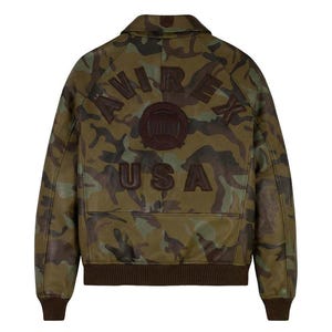May include: A camouflage-patterned leather jacket with the word "AVIREX" arched across the back, a circular emblem, and the word "USA" below. The jacket has a brown collar, cuffs, and hem.