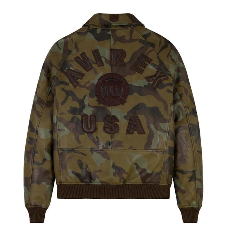 May include: A camouflage-patterned leather jacket with the word "AVIREX" arched across the back, a circular emblem, and the word "USA" below. The jacket has a brown collar, cuffs, and hem.