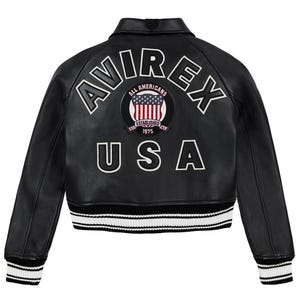 Op de afbeelding: Zwarte leren jas met witte letters en patches. De achterkant van de jas heeft het woord "AVIREX" boven een cirkelvormige patch met de Amerikaanse vlag en de woorden "ALL AMERICANS ESTABLISHED 1975". Daaronder staat het woord "USA". De jas heeft wit-zwart gestreepte manchetten en zoom.