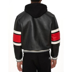 May include: Black leather jacket with a black hood, red and white striped sleeves, and a white and black striped hem. The jacket is worn with black pants. The back view of the jacket is shown.